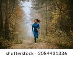 Small photo of Young woman in blue track suit running toward camera on the forest trail at autumn