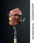 Small photo of Grilled ribeye beef steak with rosemary on a black background. Beef steak on a fork.