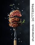 Grilled beef steak with spices on a black background. Beef steak on a fork sprinkled with rosemary and sea salt.   
