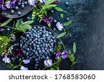Small photo of Fresh juicy blueberries on a black plate. Summer still life with blueberries, colored sweet peas and meadow grasses. View from the top.