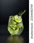 Small photo of Gin tonic with ice, rosemary, lime, and cucumber in frosted glass. Glass with a cocktail on a black background. Copy space.