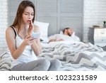 Small photo of Disloyalty. Beautiful baffled heart-broken woman reading her mans messages while he sleeping and she sitting on the bed