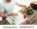 Small photo of Program of nutrition. Occupied concentrated unshaken man having breakfast by the table looking at smartphone taking vegetables.