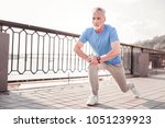 Small photo of Sport forever. Senior confident unshaken making man exercises on the quay stretching legs and looking aside.