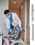 Small photo of Elderly Caucasian man in a face mask sitting in his wheelchair during the heart auscultation