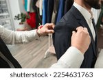 Small photo of Experienced clothier altering suit jacket of client