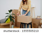 Middle age woman in casual clothes standing next to pile of boxes, packing, she's moving out from an old apartment. Sealing cardboard boxes with adhesive scotch tape. Close up, cropped, no head.