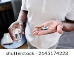 African American senior man with glass of water and three pills on hand going to take medicaments prescribed by his physician