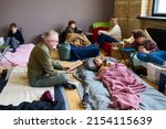 Mature man with open book reading fairy tale to his grandson lying in bed while resting in temporary shelter with other refugees
