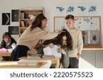 Small photo of Cruel schoolgirl laughing at classmate and pulling his hair while another boy fighting with him in classroom against African American girl