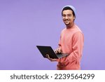 Small photo of Young successful designer or freelancer in casualwear using laptop and looking at camera with smile while standing on violet background