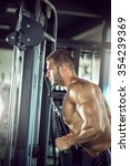 Small photo of Young adult man doing triceps rope pushdown exercise in gym.