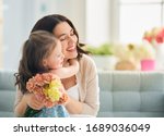 Happy mother's day! Child daughter congratulates mom and gives her flowers. Mum and girl smiling and hugging. Family holiday and togetherness.                               