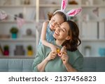 Small photo of Happy holiday! Mother and her daughter with painting eggs. Family celebrating Easter. Cute little child girl is wearing bunny ears.