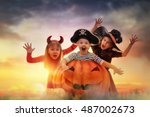 Happy brother and two sisters on Halloween. Funny kids in carnival costumes outdoors. Cheerful children and pumpkins on sunset background.