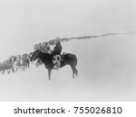 Small photo of American cowboy on horseback watches a long line of cattle plodding through snow