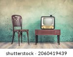Small photo of Television set receiver from 50s on wooden outdated analog TV stand and old classic chair front color textured aged concrete wall background. Vintage style filtered photo