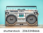 Retro outdated portable cassette tape recorder from 80s on wooden table front mint blue wall background. Vintage old style filtered photo