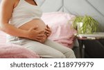 Small photo of A pregnant girl is sitting on the bed and holding her big belly. A long gestation period.