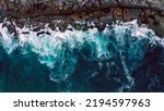 Drone view over  sea water surface the rocky shore. Top view over rolling ocean waves to the rocky shore.  Aerial view of the beautiful ocean and rocky shore with rolling waves on the summer day.