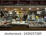 Small photo of Barcelona, Spain – April 18, 2018: Horizontal frontal view of a cod and ready meals stall, with its owners, in the old Abaceria Central Market of the Gracia neighborhood