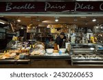 Small photo of Barcelona, Spain – April 18, 2018: Horizontal frontal view of a cod and ready meals stall, with its owner arranging the goods, in the old Abaceria Central Market of the Gracia neighborhood