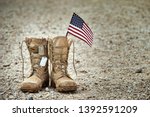 Small photo of Old military combat boots with dog tags and a small American flag. Rocky gravel background with copy space. Memorial Day, Veterans day, sacrifice concept.