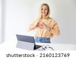 pretty young blonde woman with beautiful laugh stands by height adjustable table and shapes heart with her hands and is happy