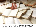 Small photo of A student or reader drowned in a mountain of books. Man's hand sticks out from the rubble of open books. Concept - preparing for exams or excess information. Selective focus.