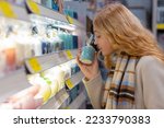 Small photo of Teenage girl smelling the scented candle at shop. Customer tries goods in the store. Portrait of young woman in shop testing perfume goods. Woman chooses aroma of candle.