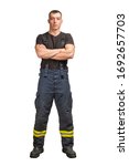Small photo of Young firefighter with folded arms wearing black t-shirt and fireproof pants with suspenders isolated on white background