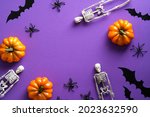 Frame of Halloween decorations on purple background. Flat lay skeletons, bats silhouettes, spiders, pumpkins. Happy Halloween concept.
