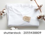 Organic cotton t-shirt with cotton flowers on white background. Flat lay, top view. Eco clothing, sustainable lifestyle, fashion concept.