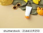 Kids sunscreen cream tube with sunglasses, panama hat, towel, sand molds on beige background.