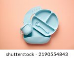 Small photo of Flat lay composition with silicone baby bib and dishware on peach color background. Serving baby food concept. Flat lay, top view