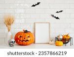 Halloween holiday concept. Empty photo frame, carved pumpkin jack-o-lantern, skull, bats on white brick  wall background