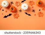 Halloween flat lay composition with pumpkins, spiders, bats, maple leaves on pastel orange background.