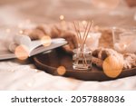 Small photo of Home perfume in glass bottle with wood sticks, scented burn candles, open paper book and knit wool textile on ray in bedroom close up. Aromatherapy cozy atmosphere lifestyle. Winter warm xmas season.