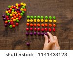 woman's hand collects even row of colorful candies on a wooden background