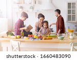 Small photo of Happy family cooking together on kitchen. Mother and daughter reading recipe to father and son. Dad and boy chopping green vegetable leaf for salad. Home recreation and food preparation on weekend