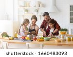 Small photo of Happy family cooking together on kitchen. Mother and daughter reading recipe to father and son. Dad and boy chopping green vegetable leaf for salad. Home recreation and food preparation on weekend
