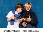 Two schoolboys playing online on smartphones devices together on blue background. New generation, kids and technology.