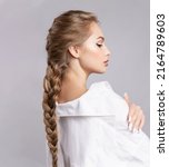 Small photo of Glamourous young blond caucasian woman with healthy shiny long hairs in pigtail hold braid in hand. Alluring female with stylish plait posing on gray studio background. Haircare treatment cosmetics ad