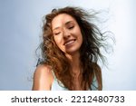 Portrait of happy young woman smiling in the sunshine on  blue background. Model with curly  hair and perfect skin. Haircare concept.