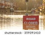 A 'Road Closed' sign partially covered in flood water lit by the evening sun