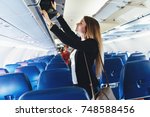 Female student putting her hand luggage into overhead locker on airplane
