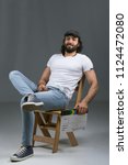 Small photo of Director man wearing a casual outfit, sitting crossed legs on a wooden chair, holding capper board and smiling