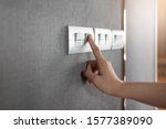 Asian female right hand is turning on or off on grey light switch over gray textile texture wall at the house or hotel. Copy space.