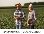 Handsome young farmer wearing straw hat laughing. Senior farmer holding straw hat in hand talking smiling. 