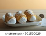 Sweet tubes filled egg white, Czech confection called Kremrole on white plate on wooden table.